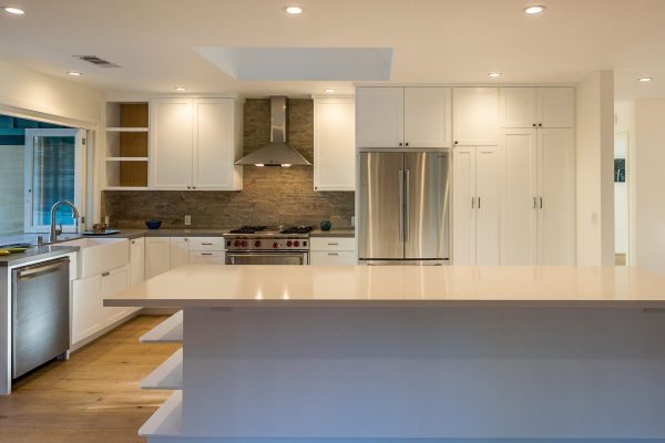 Modern kitchen with extra-large island, white shaker cabinets, stainless steel appliances, farmhouse sink, stone backsplash, and wide-plank wood flooring.