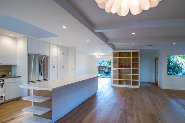 Open-concept Tampa home remodel featuring a large modern kitchen island, white cabinetry, built-in shelving, and wide-plank hardwood floors.